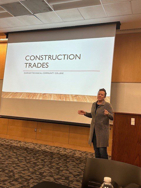 A speaker gesturing with one hand in front of a presentation slide titled "construction trades and diversity" at Durham Technical Community College.